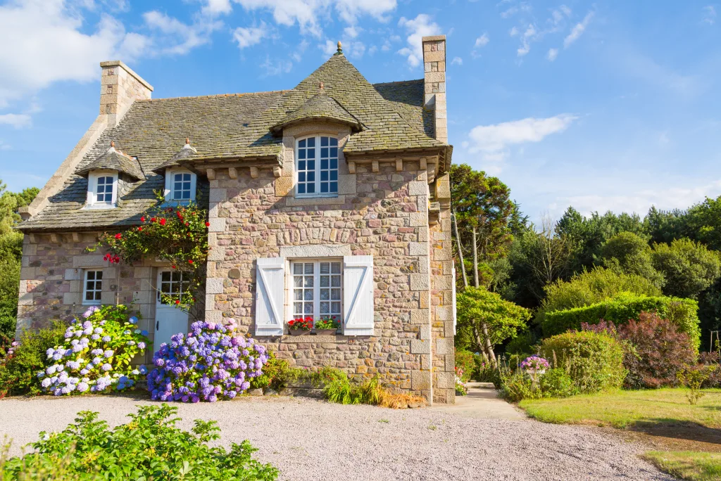 Traditional stone cottage in spring. Light blue and purple hydrangea flowers sit either side of the front door. 