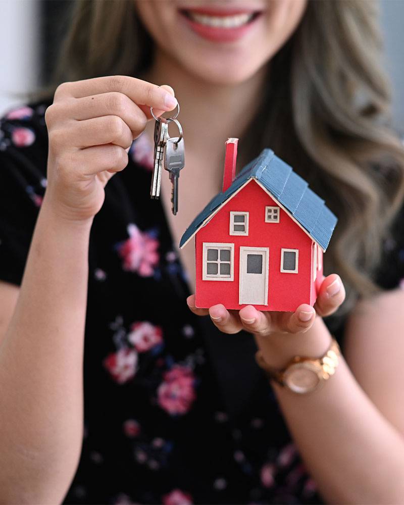 Smiling asian woman holding house model and house key in hand. R