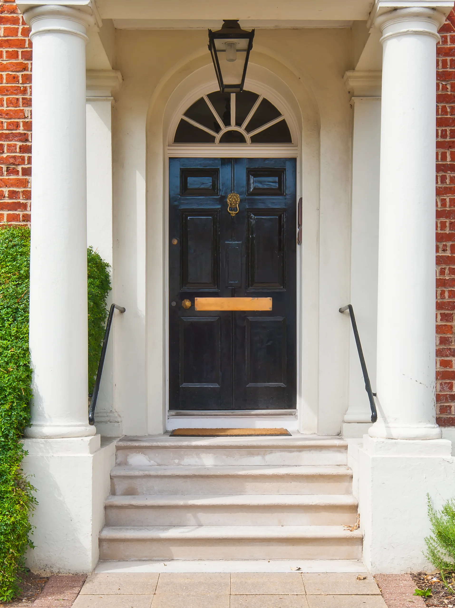 A Victorian style front door. The door is black and has grand steps and columns in front 