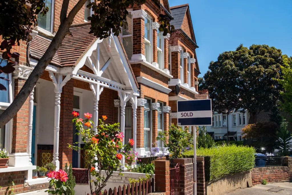 A photo looking down a street. A sold sign is visible outside the property and it is a bright and sunny day 
